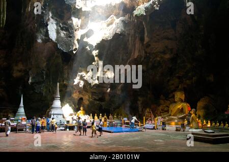 Thailand: Gläubige in der Haupthöhle von Tham Khao Luang, Phetchaburi. Tham Khao Luang ist eine große Höhle, die aus drei miteinander verbundenen Kammern besteht und sich durch viele hängende Stalaktiten und Buddha-Bilder auszeichnet, einschließlich eines phra non oder liegenden Buddha. Das Hauptbronzebild wurde auf Befehl von König Chulalongkorn (Rama V) gegossen und seinen berühmten Vorgängern, den Königen Rama III. Und Rama IV., gewidmet Es gibt eine natürliche Öffnung in der Decke der zweiten, Hauptkammer, durch die Tageslicht strömt und die Bilder im Inneren erhellt. Stockfoto