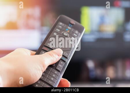 Nahaufnahme der Hand der Frau, die die Fernbedienung vor dem Fernseher hält Stockfoto