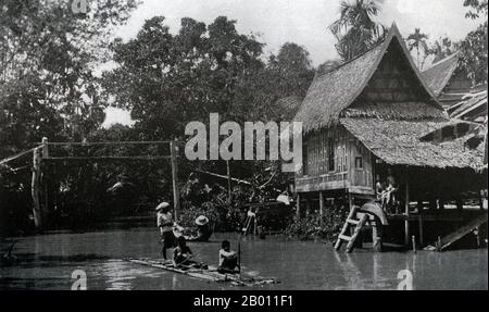 Thailand: Ein traditionelles siamesisches Haus auf Stelzen an einem Kanal in Bangkok Noi, c. 1900. Um die Wende des 20. Jahrhunderts waren die meisten Siamesen Reisbauern, die entlang der Wasserwege lebten und arbeiteten. Jeder Haushalt hatte ein Boot, von dem schätzungsweise 600,000 die Kanäle und Flüsse von Bangkok befuhren. Rudern wurde von der Rückseite des Bootes aus durchgeführt. Die meisten Häuser wurden aus Holz und Bambus gebaut und auf Stelzen mit einer Leiter zum Wasser gebaut. Stockfoto