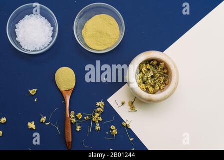 Diese Gesichtspackung entfernt abgestorbene Haut. Kollagenpulver oder gelber Ton auf klassisch blauem und beigefarbenem Hintergrund mit Holzlöffel. Flacher Laienstil. Home Skin Auto Stockfoto