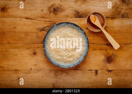 Eine nahrhafte Porridschüssel und eine Schüssel mit goldenem Sirup mit einem Holzlöffel auf Holzgrund Stockfoto