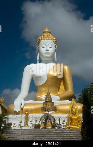 Thailand: Riesige Buddha-Statue mit Blick auf das Chiang Mai-Tal, Wat Phrathat Doi Kham, Chiang Mai. Wat Phrathat Doi Kham oder ‘Tempel des Goldenen Berges’, befindet sich in Tambon Mae Hia, etwa 10 km südlich der Altstadt von Chiang Mai, im schutze von Doi Suthep. Tempelrekorde behaupten, dass der Tempel über 1,300 Jahre ‘bis 687 u.Z.’ zurückreicht, während der Zeit vor LAN Na, als die Region von der einheimischen Animstin Lawa bewohnt wurde. Chiang Mai (was „neue Stadt“ bedeutet), manchmal auch als „Chiengmai“ oder „Chiangmai“ geschrieben, ist die größte und kulturell bedeutsamste Stadt im Norden Thailands. Stockfoto