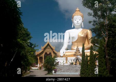 Thailand: Riesige Buddha-Statue mit Blick auf das Chiang Mai-Tal, Wat Phrathat Doi Kham, Chiang Mai. Wat Phrathat Doi Kham oder ‘Tempel des Goldenen Berges’, befindet sich in Tambon Mae Hia, etwa 10 km südlich der Altstadt von Chiang Mai, im schutze von Doi Suthep. Tempelrekorde behaupten, dass der Tempel über 1,300 Jahre ‘bis 687 u.Z.’ zurückreicht, während der Zeit vor LAN Na, als die Region von der einheimischen Animstin Lawa bewohnt wurde. Chiang Mai (was „neue Stadt“ bedeutet), manchmal auch als „Chiengmai“ oder „Chiangmai“ geschrieben, ist die größte und kulturell bedeutsamste Stadt im Norden Thailands. Stockfoto