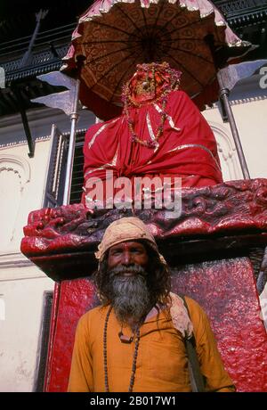 Nepal: Sadhu vor der Hanuman-Statue im Hanuman Dhoka Durbar (Hanuman Royal Palace), Kathmandu. Sie sind, verschiedentlich, als Sadhus (Heilige oder 'gute'), Yogis (asketische Praktizierende) bekannt, Fakiren (asketischer Sucher nach der Wahrheit) und Sannyasine (wandernde Bettelmönchen und Asketen). Sie sind die asketischen – und oft exzentrischen – Praktizierenden einer strengen Form des Hinduismus. Geschworen, irdische Wünsche abzuwerfen, entscheiden sich manche dafür, als Anchoriten in der Wildnis zu leben. Andere sind weniger pensioniert, vor allem in den Städten und Tempeln des nepalesischen Kathmandu-Tals. Stockfoto