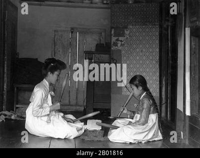 Korea: Zwei Frauen, die schwere Pangmangi-Schlagstöcke verwenden, um Kleidung zu glätten, c. 1910. In Korea galt das Trommeln traditioneller Bügelstöcke traditionell als ein fröhlicher Klang, ein Symbol für ein sicheres Zuhause. Zwei Frauen knieten auf den Boden, einander gegenübergestellt über einen glättenden Stein oder Tatumi-tol, einen Pangmangi-Schläger in jeder Hand, und schlugen einen Rhythmus auf das Tuch. Ein koreanischer Tatumi-tol Granit- oder Marmorblock war ein geschätzter Familienbesitz, vielleicht mit geschnitzter Dekoration, besonders auf der Unterseite, so dass das Design sichtbar war, wenn es kopfüber gelagert wurde, um die glatte Oberseite zu schützen. Stockfoto