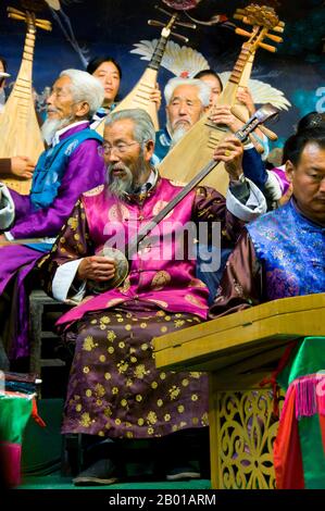 China: Ein Mann spielt einen Sanxian, das Naxi (Nakhi) Folk Orchestra, die Naxi-Orchesterhalle, Lijiang Old Town, Provinz Yunnan. Naxi-Musik ist 500 Jahre alt und hat mit ihrer Mischung aus literarischen Texten, poetischen Themen und musikalischen Stilen der Tang-, Song- und Yuan-Dynastien sowie einigen tibetischen Einflüssen einen eigenen, einzigartigen Stil und Züge entwickelt. Es gibt drei Hauptstile: Baisha, Dongjing und Huangjing, alle mit traditionellen chinesischen Instrumenten. Die Naxi oder Nakhi sind eine ethnische Gruppe, die am Fuße des Himalaya im Nordwesten der Provinz Yunnan lebt. Stockfoto