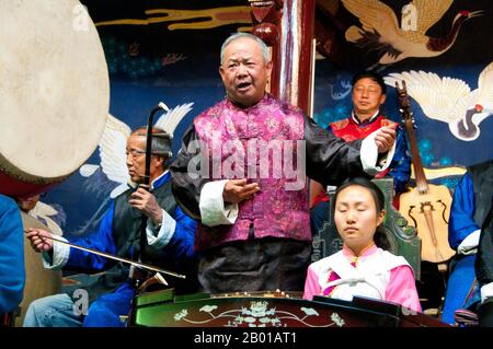 China: Ein altes Gedicht rezitieren, das Naxi Folk (Nakhi) Orchester, Naxi Orchester Halle, Lijiang Altstadt, Provinz Yunnan. Naxi-Musik ist 500 Jahre alt und hat mit ihrer Mischung aus literarischen Texten, poetischen Themen und musikalischen Stilen der Tang-, Song- und Yuan-Dynastien sowie einigen tibetischen Einflüssen einen eigenen, einzigartigen Stil und Züge entwickelt. Es gibt drei Hauptstile: Baisha, Dongjing und Huangjing, alle mit traditionellen chinesischen Instrumenten. Die Naxi oder Nakhi sind eine ethnische Gruppe, die am Fuße des Himalaya im Nordwesten der Provinz Yunnan lebt. Stockfoto