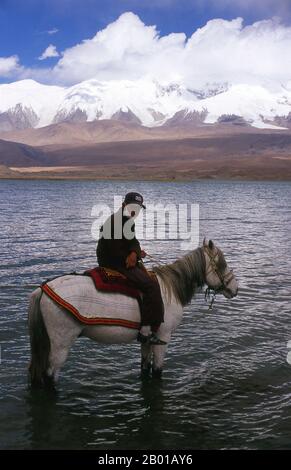 China: Kirgisische Reiter am Karakul-See auf dem Karakorum Highway, Xinjiang. Zwei kleine Siedlungen kirgisischer (kirgisischer oder kirgisischer) Nomaden liegen am Karakul-See hoch oben im Pamir-Gebirge. Die Besucher können in einem ihrer Mobilheime oder Jurten übernachten – Kirgisen kommen auf Reisende zu und bieten an, diese Unterkunft zu arrangieren. Die Kirgisen bilden eine der 56 Volksgruppen, die von der Volksrepublik China offiziell anerkannt werden. In China gibt es mehr als 145.000 Kirgisen. Stockfoto