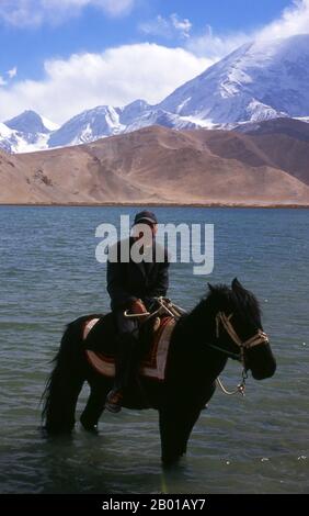 China: Kirgisische Reiter am Karakul-See auf dem Karakorum Highway, Xinjiang. Zwei kleine Siedlungen kirgisischer (kirgisischer oder kirgisischer) Nomaden liegen am Karakul-See hoch oben im Pamir-Gebirge. Die Besucher können in einem ihrer Mobilheime oder Jurten übernachten – Kirgisen kommen auf Reisende zu und bieten an, diese Unterkunft zu arrangieren. Die Kirgisen bilden eine der 56 Volksgruppen, die von der Volksrepublik China offiziell anerkannt werden. In China gibt es mehr als 145.000 Kirgisen. Stockfoto