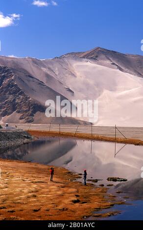 China: Touristen in der Nähe des Kangxiwa Flusses hoch oben im Pamir Gebirge, Karakorum Highway, Xinjiang. Die Pamir-Berge sind eine Gebirgskette in Zentralasien, die durch die Kreuzung oder den Knoten der Himalaya-, Tian Shan-, Karakoram-, Kunlun- und Hindu-Kush-Gebirge gebildet wird. Sie gehören zu den höchsten Bergen der Welt und sind seit viktorianischer Zeit als „Dach der Welt“ bekannt, eine wahrscheinliche Übersetzung aus dem Persischen. Der Zhongba Gonglu oder Karakoram Highway ist ein Ingenieurswunder, das 1986 eröffnet wurde und die höchste asphaltierte Straße der Welt bleibt. Sie verbindet China und Pakistan. Stockfoto