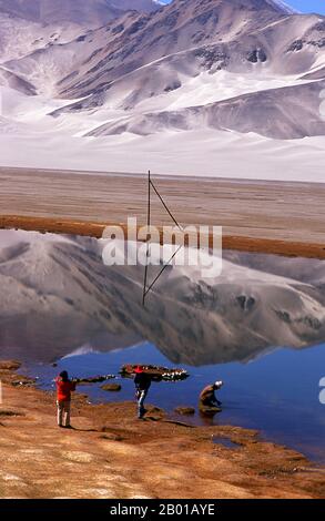 China: Touristen in der Nähe des Kangxiwa Flusses hoch oben im Pamir Gebirge, Karakorum Highway, Xinjiang. Die Pamir-Berge sind eine Gebirgskette in Zentralasien, die durch die Kreuzung oder den Knoten der Himalaya-, Tian Shan-, Karakoram-, Kunlun- und Hindu-Kush-Gebirge gebildet wird. Sie gehören zu den höchsten Bergen der Welt und sind seit viktorianischer Zeit als „Dach der Welt“ bekannt, eine wahrscheinliche Übersetzung aus dem Persischen. Der Zhongba Gonglu oder Karakoram Highway ist ein Ingenieurswunder, das 1986 eröffnet wurde und die höchste asphaltierte Straße der Welt bleibt. Sie verbindet China und Pakistan. Stockfoto