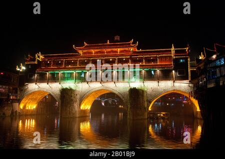 China: Hong Qiao Brücke bei Nacht, Fenghuangs berühmte überdachte Brücke, Fenghuang, Provinz Hunan. Fenghuang ist Chinesisch für Phoenix und bezieht sich auf den mythischen heiligen feuervogel, der in den Mythologien der Peter, Griechen, Römer, Ägypter, Chinesen, Und (nach Sanchuniathon) die Phönizier. Die Legende besagt, dass zwei Phönixe, die die Stadt entdeckten, einige Zeit über dem Kopf schwebten, bevor sie widerwillig wegflogen. Die Stadt Fenghuang ist eine gut erhaltene antike Stadt, die angeblich aus dem Jahr 248 v. Chr. stammt. Hier leben die Minderheiten Miao und Tujia. Stockfoto