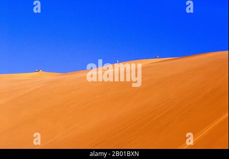 China: Wanderer auf den Sanddünen von Mingsha Shan (Mingsha Hills) in der Kumtagh-Wüste, Provinz Gansu. Mingsha Shan (Singende Sanddünen) liegen etwa 4km südlich von Dunhuang. Sie sind die größten und eindrucksvollsten Sanddünen in China. Die Hauptdünen erheben sich zwischen 250m und 300m. Sie werden ‘Singing Sands’ genannt, weil die sich verschiebenden Sandkörner bei starken Winden ein brummendes Geräusch verursachen. Die Kumtagh-Wüste ist ein Teil der Taklamakan-Wüste, die östlich-südöstlich der Wüste Lop liegt. Stockfoto