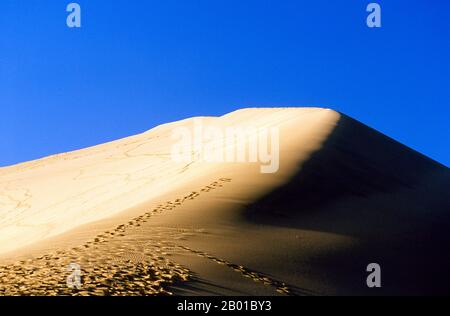 China: Die singenden Sanddünen von Mingsha Shan (Mingsha Hills) in der Kumtagh-Wüste, Provinz Gansu. Mingsha Shan (Singende Sanddünen) liegen etwa 4km südlich von Dunhuang. Sie sind die größten und eindrucksvollsten Sanddünen in China. Die Hauptdünen erheben sich zwischen 250m und 300m. Sie werden ‘Singing Sands’ genannt, weil die sich verschiebenden Sandkörner bei starken Winden ein brummendes Geräusch verursachen. Die Kumtagh-Wüste ist ein Teil der Taklamakan-Wüste, die östlich-südöstlich der Wüste Lop liegt. Stockfoto