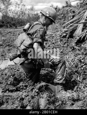 Vietnam: Ein Infanterist der US-Armee, der im Schlamm des Mekong-Deltas, c. 1966. Der zweite Indochinakrieg, in Amerika als Vietnamkrieg bekannt, war ein militärischer Konflikt aus der Zeit des Kalten Krieges, der sich vom 1. November 1955 bis zum Sturz Saigons am 30. April 1975 in Vietnam, Laos und Kambodscha ereignete. Dieser Krieg folgte dem ersten Indochina-Krieg und wurde zwischen Nordvietnam, unterstützt von seinen kommunistischen Verbündeten, und der Regierung von Südvietnam, unterstützt von den USA und anderen antikommunistischen Nationen, geführt. Die US-Regierung betrachtete die Beteiligung am Krieg als eine Möglichkeit, eine kommunistische Übernahme zu verhindern. Stockfoto