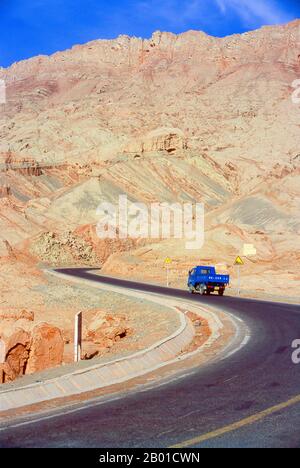 China: Straße neben dem Dorf Tuyoq in der Nähe von Turpan, Provinz Xinjiang. Tuyoq oder Tuyugou ist ein altes Oasendorf in der Taklamakan Wüste, 70 km östlich von Turpan in einem üppigen Tal, das in die Flaming Mountains schneidet, mit einer gut erhaltenen uigurischen Ausrichtung. Es ist berühmt für seine kernlosen Trauben und eine Reihe von alten buddhistischen Meditationshöhlen in der Nähe mit Fresken, die bekannteste sind die Bezeklik Thousand Buddha Höhlen. Stockfoto