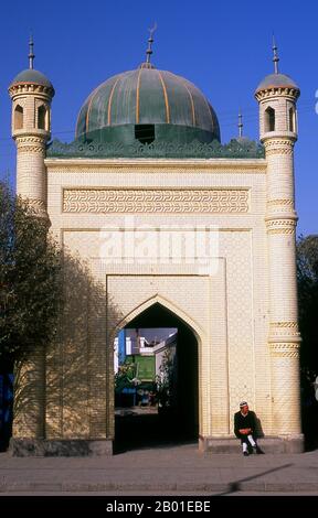 China: Uigurischer Mann vor dem Eingang einer Moschee in der Altstadt von Kuqa, Provinz Xinjiang. Die antike Oasenstadt Kuqa (Kuche), die jetzt von Korla im Osten und Aksu im Westen überschattet wird, war einst ein wichtiger Halt an der nördlichen Seidenstraße. Es wurde erstmals von Han Chinas Kontrolle erobert, als es 91 CE vom unbezwingbaren General Ban Chao erobert wurde. Im 4. Jahrhundert war sie zu einem wichtigen Zentrum der tocharischen Zivilisation geworden, das nicht nur auf der nördlichen Seidenstraße, sondern auch auf kleineren Routen nach Dzungaria im Norden und nach Khotan im Süden saß. Stockfoto