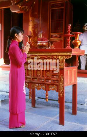 Vietnam: Eine Frau an einem Altar hinter dem Großen Haus der Zeremonien, dem Tempel der Literatur (Van Mieu), Hanoi. Der Literaturtempel oder Van Mieu ist einer der bedeutendsten kulturellen Schätze Vietnams. Der Tempel wurde 1070 von König Ly Thanh Tong aus der frühen Ly-Dynastie gegründet und war ursprünglich Konfuzius und Chu Cong gewidmet, einem Mitglied der chinesischen Königsfamilie, dem viele der Lehren, die Konfuzius fünfhundert Jahre später entwickelte, zugeschrieben wurden. Die Stätte wurde von Geomancern der Ly-Dynastie ausgewählt, um im Einklang mit dem taoistischen Bich Cau-Tempel und der buddhistischen Einsäulenpagode zu stehen. Stockfoto