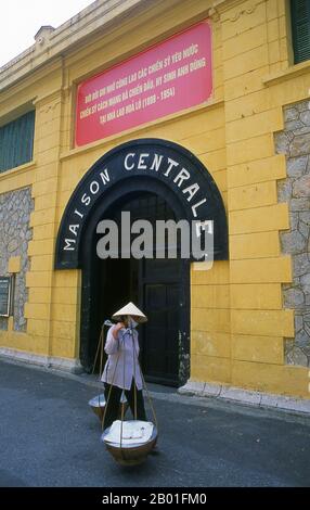 Vietnam: Ein Verkäufer geht vorbei am Eingang zum Hoa Lo Gefängnismuseum (das alte französische Maison Centrale), Hanoi. Die französische Kolonialverwaltung baute 1896 das Hoa Lo Gefängnis. Ursprünglich sollten 450 Gefangene festgehalten werden, und in den 1930er Jahren war die Zahl der Inhaftierten auf fast 2.000 angestiegen, die politische Gefangene mit großer Mehrheit. Das Hoa Lo Gefängnis wurde während des Zweiten Indochina-Krieges als Ort der Inhaftierung für niedergeschlagene US-Piloten bekannt, die das Gefängnis ironischerweise „Hanoi Hilton“ nannten. Stockfoto