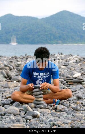 Thailand: Besucher am Kieselstrand, Ko hin Ngam, Ko Tarutao Marine National Park. Ko hin Ngam bedeutet auf Thai „Insel der schönen Steine“, und der kleine Strand ist mit glatten schwarzen Steinen in verschiedenen Formen bedeckt und mit charakteristischen Mustern bedeckt. Der Marine-Nationalpark Ko Tarutao besteht aus 51 Inseln in zwei Hauptgruppen, die über die Andamanensee im südlichsten Thailand verstreut sind. Nur sieben der Inseln haben jede Größe, einschließlich Ko Tarutao im Osten und Ko Adang-Ko Rawi im Westen. Nur 5 Meilen (8km km) südlich liegt die Meeresgrenze mit Malaysias gefeiertem Langkawi-Archipel. Stockfoto