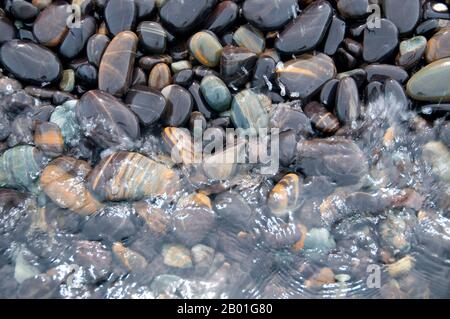 Thailand: Gestreifte Kiesel, Ko hin Ngam, Ko Tarutao Marine Nationalpark. Ko hin Ngam bedeutet auf Thai „Insel der schönen Steine“, und der kleine Strand ist mit glatten schwarzen Steinen in verschiedenen Formen bedeckt und mit charakteristischen Mustern bedeckt. Der Marine-Nationalpark Ko Tarutao besteht aus 51 Inseln in zwei Hauptgruppen, die über die Andamanensee im südlichsten Thailand verstreut sind. Nur sieben der Inseln haben jede Größe, einschließlich Ko Tarutao im Osten und Ko Adang-Ko Rawi im Westen. Nur 5 Meilen (8km km) südlich liegt die Meeresgrenze mit Malaysias gefeiertem Langkawi-Archipel. Stockfoto