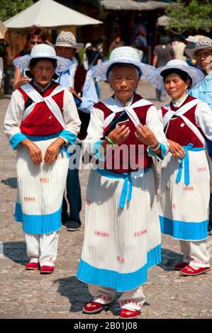 China: Naxi-Frauen tanzen auf dem Alten Marktplatz (Sifang Jie), in der Altstadt von Lijiang, Provinz Yunnan. Die Naxi oder Nakhi sind eine ethnische Gruppe, die in den Ausläufern des Himalaya im Nordwesten der Provinz Yunnan und im Südwesten der Provinz Sichuan in China lebt. Man geht davon aus, dass die Naxi ursprünglich aus Tibet stammen und bis vor kurzem die Landhandelsverbindungen mit Lhasa und Indien aufrechterhalten haben. Die Naxi gehören zu den 56 ethnischen Gruppen, die von der Volksrepublik China offiziell anerkannt wurden. Die Naxi sind traditionell Anhänger der Dongba-Religion. Stockfoto