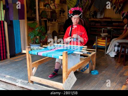 China: Mosuo Weben in der Altstadt von Lijiang, Provinz Yunnan. Die Mosuo (auch Moso oder Musuo), die sich selbst oft als Na bezeichnet, sind eine kleine ethnische Gruppe, die in den Provinzen Yunnan und Sichuan in der Nähe der Grenze zu Tibet lebt. Mit einer Bevölkerung von etwa 40.000 leben die meisten von ihnen in der Region Yongning und rund um den Lugu-See, hoch oben im tibetischen Himalaya. Obwohl sich die Mosuo kulturell von den Nakhi unterscheiden, sieht die chinesische Regierung sie als Mitglieder der Nakhi-Minderheit (auch bekannt als Naxi) an. Die Altstadt von Lijiang reicht mehr als 800 Jahre zurück und war einst eine wichtige Stadt. Stockfoto