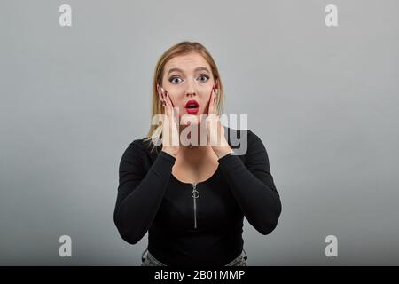 Junge blonde Mädchen in schwarzer Jacke schockierte Frau hält ihre Hände auf den Wangen Stockfoto