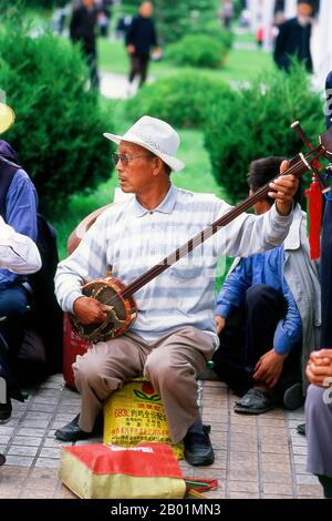 China: Ein Mann spielt Sanxian in einem Park in Wuwei, Provinz Gansu. Die Stadt Wuwei hat eine Bevölkerung von etwa 500.000, hauptsächlich Han-Chinesen, aber mit sichtbaren Zahlen von Hui sowie Mongolen und Tibetern. Früher hieß es Liangzhou. Er dominiert das östliche Ende des Hexi-Korridors und spielt seit langem eine wichtige Rolle auf dieser wichtigen Handelsroute. WuWeis berühmtestes historisches Artefakt, das gefeierte Bronzepferd der Han-Dynastie (206 v. Chr. - 220 n. Chr.), bekannt als das fliegende Pferd von Gansu, wurde hier in einem Grab unter dem Leitai-Tempel (Leitai Si) im nördlichen Teil der Stadt entdeckt. Stockfoto