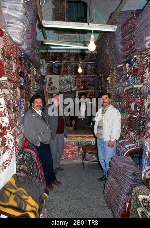 Syrien: Ein Teppichladen in Aleppos altem Souk (Basar). Aleppos großer Basar (auf Arabisch Suq oder Souk), wie wir ihn heute kennen, wurde zuerst von den ägyptischen Mameluken, die die Mongolen vertrieben, und dann, nach 1516, von den Türken, die Aleppo in das Osmanische Reich einverleibten, wiederaufgebaut. Aleppo, die zweite Stadt Syriens und möglicherweise die am längsten bewohnte Siedlung der Welt, ist von ehrwürdigem Alter. So alt, dass sein arabischer Name Halab erstmals in semitischen Texten des dritten Jahrtausends v. Chr. erwähnt wird. Stockfoto