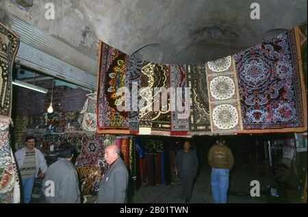 Syrien: Teppiche hängen auf dem alten Großen Basar (Souk), Aleppo. Aleppos großer Basar (auf Arabisch Suq oder Souk), wie wir ihn heute kennen, wurde zuerst von den ägyptischen Mameluken, die die Mongolen vertrieben, und dann, nach 1516, von den Türken, die Aleppo in das Osmanische Reich einverleibten, wiederaufgebaut. Aleppo, die zweite Stadt Syriens und möglicherweise die am längsten bewohnte Siedlung der Welt, ist von ehrwürdigem Alter. So alt, dass sein arabischer Name Halab erstmals in semitischen Texten des dritten Jahrtausends v. Chr. erwähnt wird. Stockfoto