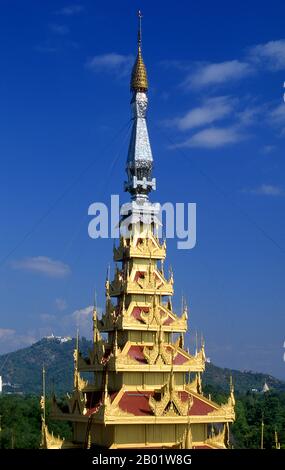 Birma/Myanmar: Ein raffiniertes Dach im Palast von König Mindon, Mandalay (rekonstruiert), mit dem Hügel Mandalay im Hintergrund. Die fast 3 km langen Mauern des Fort Mandalay umschließen den Palast von König Mindon. Die Wände ragen 8 m hoch. Der Palast wurde zwischen 1857 und 1859 als Teil der Gründung der neuen königlichen Hauptstadt Mandalay durch König Mindon errichtet. Der Plan des Mandalay Palace folgt weitgehend dem traditionellen burmesischen Palastdesign in einer ummauerten Festung, die von einem Graben umgeben ist. Der Palast selbst befindet sich in der Mitte der Zitadelle und zeigt nach Osten. Alle Gebäude des Palastes sind ein Stockwerk hoch Stockfoto