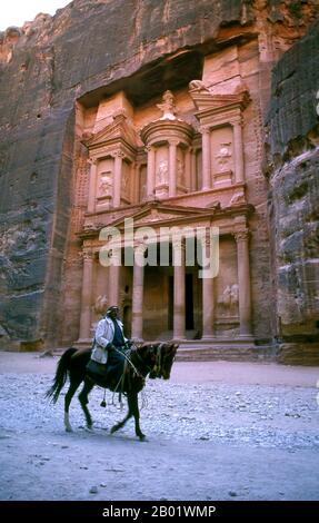 Jordanien: Ein arabischer Reiter vor Al Khazneh (dem Finanzministerium), Petra. Al Khazneh („die Schatzkammer“) ist eines der raffiniertesten Gebäude in der alten jordanischen Stadt Petra. Wie bei den meisten anderen Gebäuden in dieser antiken Stadt, einschließlich des Klosters, wurde auch dieses Gebäude aus einer Sandsteinwand gemeißelt. Es hat klassisch griechisch beeinflusste Architektur. Petra wurde im 4. Jahrhundert v. Chr. von den nabatäischen Arabern als Stadt gegründet und verdankt seine Geburt und seinen Wohlstand der Tatsache, dass es der einzige Ort mit klarem und reichlich Wasser zwischen den Hijaz-Handelszentren war. Stockfoto