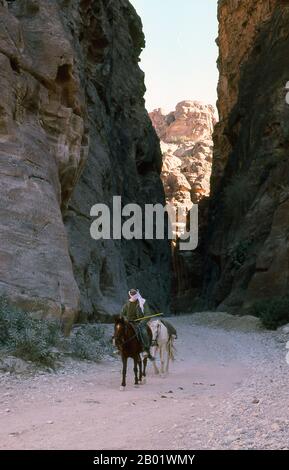 Jordanien: Arabischer Reiter im Siq (Schacht), der zur antiken Stadt Petra führt. Der Siq oder al-Siq ist der Haupteingang zur antiken Stadt Petra im südlichen Jordanien. Die dunkle, schmale Schlucht (an einigen Stellen nicht mehr als 3 Meter breit) windet sich etwa 1,5 km und endet bei Petras aufwändigster Ruine, Al Khazneh (die Schatzkammer). Petra wurde im 4. Jahrhundert v. Chr. von den nabatäischen Arabern als Stadt gegründet und verdankt seine Geburt und seinen Wohlstand der Tatsache, dass es der einzige Ort mit klarem und reichlich Wasser zwischen den Hidschas-Handelszentren Mekka und Medina und Palästina war. Stockfoto