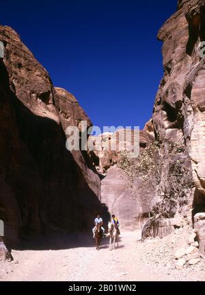 Jordanien: Junge Reiter im Siq (Schacht), der zur antiken Stadt Petra führt. Der Siq oder al-Siq ist der Haupteingang zur antiken Stadt Petra im südlichen Jordanien. Die dunkle, schmale Schlucht (an einigen Stellen nicht mehr als 3 Meter breit) windet sich etwa 1,5 km und endet bei Petras aufwändigster Ruine, Al Khazneh (die Schatzkammer). Petra wurde im 4. Jahrhundert v. Chr. von den nabatäischen Arabern als Stadt gegründet und verdankt seine Geburt und seinen Wohlstand der Tatsache, dass es der einzige Ort mit klarem und reichlich Wasser zwischen den Hidschas-Handelszentren Mekka und Medina und Palästina war. Stockfoto