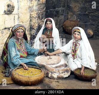 Palästina: Drei palästinensische Frauen mahlen Mais, Ramallah, um 1900. Palästina ist ein Name für die geografische Region zwischen dem Mittelmeer und dem Jordan. Die Region ist auch als das Land Israel, das Heilige Land und die Südlevante bekannt. 1832 wurde Palästina von Mohammed Alis Ägypten erobert, aber 1840 intervenierte Großbritannien und gab die Kontrolle über die Levante an die Osmanen zurück, als Gegenleistung für weitere Kapitulationen. Am Ende des 19. Jahrhunderts begann die zionistische Einwanderung und die Wiederbelebung der hebräischen Sprache. Stockfoto