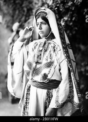 Palästina: Eine palästinensische Frau von Ramallah in einem bestickten Kleid, um 1915. Palästina ist ein Name für die geografische Region zwischen dem Mittelmeer und dem Jordan. Die Region ist auch als das Land Israel, das Heilige Land und die Südlevante bekannt. 1832 wurde Palästina von Mohammed Alis Ägypten erobert, aber 1840 intervenierte Großbritannien und gab die Kontrolle über die Levante an die Osmanen zurück, als Gegenleistung für weitere Kapitulationen. Am Ende des 19. Jahrhunderts begann die zionistische Einwanderung und die Wiederbelebung der hebräischen Sprache. Stockfoto