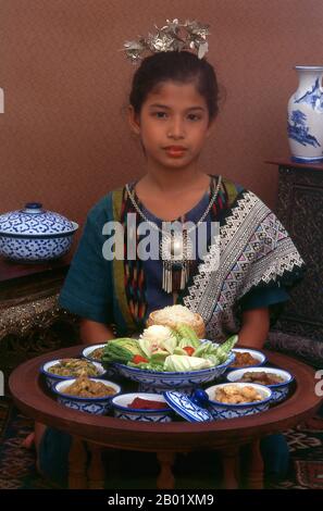 Thailand: Ein Mädchen in traditioneller Lanna-Kleidung probiert ein khantoke-Dinner in Chiang Mai, Nordthailand. Nordthailand hat das kulinarische Erbe des einst mächtigen Königreichs Lan Na geerbt, mit Verbindungen zum benachbarten Burma und zur chinesischen Provinz Yunnan. Ein bemerkenswertes Merkmal ist die weit verbreitete Verwendung von Tomaten in Currys und anderen gekochten Gerichten – anderswo in Thailand wird die Tomate normalerweise als Salatgemüse angesehen. Zu den besonderen Gerichten gehört khao Soja, ein saftiges Nudelgericht, das von muslimischen Karawaneern aus China eingeführt wird. Stockfoto