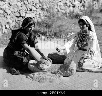 Palästina: Zwei palästinensische Frauen, die Weizen mahlen, um 1920. Palästina ist ein Name für die geografische Region zwischen dem Mittelmeer und dem Jordan. Die Region ist auch als das Land Israel, das Heilige Land und die Südlevante bekannt. 1832 wurde Palästina von Mohammed Alis Ägypten erobert, aber 1840 intervenierte Großbritannien und gab die Kontrolle über die Levante an die Osmanen zurück, als Gegenleistung für weitere Kapitulationen. Am Ende des 19. Jahrhunderts begann die zionistische Einwanderung und die Wiederbelebung der hebräischen Sprache. Stockfoto