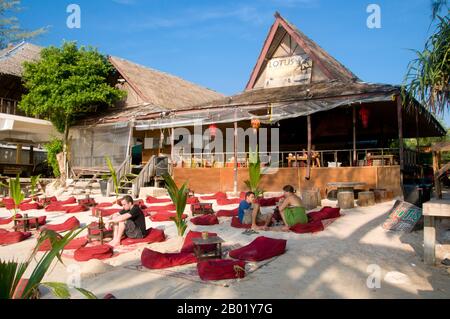 Thailand: Gäste vor einem Restaurant bei Sonnenuntergang, hat Sai Ri, Ko Tao (Turtle Island), Südthailand. Ko Tao oder Turtle Island, die sich mitten im Golf von Thailand befindet, wurde von den frühen Siedlern nach der buckeligen, schildkrötenähnlichen Form der Insel benannt, obwohl sie auch ein bedeutender Brutplatz für Karettschildkröten und Grüne Schildkröten ist. Die Wirtschaft der Insel, die bis auf die vorübergehenden Fischer einst unbewohnt war, dreht sich heute fast ausschließlich um Tourismus und Tauchen. Die rasche Entwicklung des Tourismus in den letzten Jahren hat sich negativ auf die Schildkrötenzucht ausgewirkt. Stockfoto