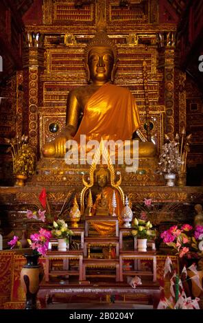 Thailand: Buddha-Figur im alten Viharn, Wat Hang Dong, Chiang Mai, Nord-Thailand. Wat Hang Dong ist ein typisches Beispiel für traditionelle LAN Na Tempelarchitektur. Der alte Viharn in diesem Tempel ist etwas aufwändiger als sein Gegenstück im nahe gelegenen Wat Ton Kwen, ist aber in Form, Stil und Aussehen im Wesentlichen ähnlich. Auch dunkel und intim, mit einem niedrigen, geschwungenen, dreistöckigen Dach, beherbergt der Viharn eine Sammlung von Buddha-Bildern, von denen mindestens zwei – rechts und links vom Hauptbild des Buddha – im Stil von Lao und doch irgendwie seltsam primitiv sind. Stockfoto