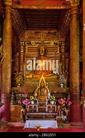 Thailand: Buddha-Figur im alten Viharn, Wat Hang Dong, Chiang Mai, Nord-Thailand. Wat Hang Dong ist ein typisches Beispiel für traditionelle LAN Na Tempelarchitektur. Der alte Viharn in diesem Tempel ist etwas aufwändiger als sein Gegenstück im nahe gelegenen Wat Ton Kwen, ist aber in Form, Stil und Aussehen im Wesentlichen ähnlich. Auch dunkel und intim, mit einem niedrigen, geschwungenen, dreistöckigen Dach, beherbergt der Viharn eine Sammlung von Buddha-Bildern, von denen mindestens zwei – rechts und links vom Hauptbild des Buddha – im Stil von Lao und doch irgendwie seltsam primitiv sind. Stockfoto