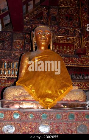 Thailand: Buddha-Figur im alten Viharn, Wat Hang Dong, Chiang Mai, Nord-Thailand. Wat Hang Dong ist ein typisches Beispiel für traditionelle LAN Na Tempelarchitektur. Der alte Viharn in diesem Tempel ist etwas aufwändiger als sein Gegenstück im nahe gelegenen Wat Ton Kwen, ist aber in Form, Stil und Aussehen im Wesentlichen ähnlich. Auch dunkel und intim, mit einem niedrigen, geschwungenen, dreistöckigen Dach, beherbergt der Viharn eine Sammlung von Buddha-Bildern, von denen mindestens zwei – rechts und links vom Hauptbild des Buddha – im Stil von Lao und doch irgendwie seltsam primitiv sind. Stockfoto