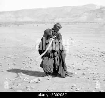 Arabien: Eine Beduinenfrau, die einen Schwerttanz für eine Hochzeit aufführt, um 1900-1920. Beduinen sind Teil einer überwiegend in der Wüste lebenden arabischen ethnischen Gruppe, die traditionell in Stämme oder Clans unterteilt ist, die auf Arabisch als ʿašāʾir bekannt sind. Der Begriff Beduin leitet sich von einer Pluralform des arabischen Wortes badawī ab, wie es in umgangssprachlichen Dialekten ausgesprochen wird. Der arabische Begriff badawī leitet sich vom Wort bādiyah ab, was semiaride Wüste bedeutet (im Gegensatz zu ṣaḥarāʾ, was Wüste bedeutet). Ab dem späten 19. Jahrhundert begannen viele Beduinen unter britischer Herrschaft in ein seminomadisches Leben zu übergehen. Stockfoto