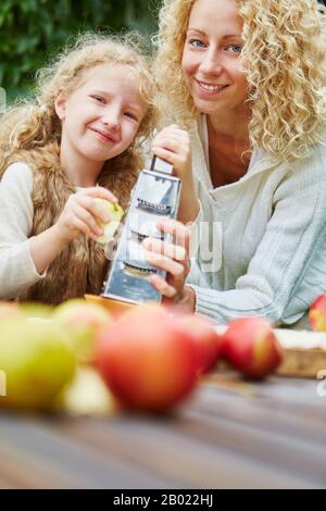 Glückliche Mutter und lächelnde Tochter reiben apfel für einen Kuchen Stockfoto