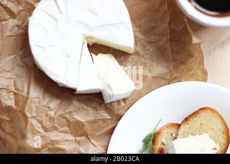 Französischer Käse. Käsebraut in Packpapier auf dem Tisch mit Toast und Tasse Kaffee. Styling von Lebensmitteln. Traditionelle französische Produkte. Stockfoto