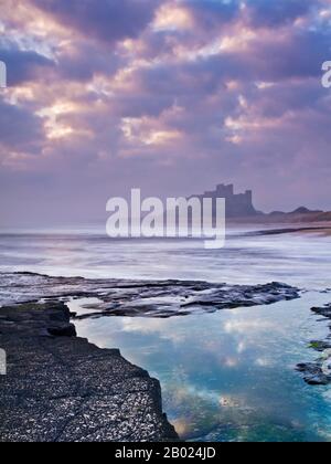 Bamburgh Castle an der ersten Ampel aus einem Whin Sill Rock Regal nördlich des Schlosses, Northumberland, England Stockfoto