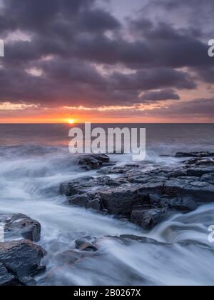 Sonnenaufgang über den vulkanischen Doleritfelsen von Craster, Northumberland, England Stockfoto