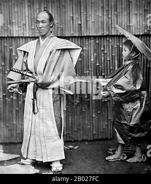 Japan: Ein Samurai posiert mit zwei Schwertern und einem Begleiter, um 1890. Samurai, auf Japanisch meist als Bushi oder Buke bezeichnet, waren der militärische Adel des mittelalterlichen und frühmodernen Japans. Am Ende des 12. Jahrhunderts wurden Samurai fast vollständig zum Synonym für Bushi, und das Wort war eng mit der mittleren und oberen Ebene der Kriegerklasse verbunden. Die Samurai folgten einer Reihe von Regeln, die als bushidō bekannt wurden. Während die Samurai weniger als 10 % der japanischen Bevölkerung ausmachen, finden sich ihre Lehren heute noch sowohl im Alltag als auch in der japanischen Kampfkunst. Stockfoto