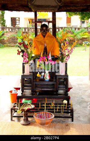 Thailand: Statue und Schrein für einen alten Abt von Wat Ton Kwen, Chiang Mai. Wat Ton Kwen, früher als Wat Inthrawat bekannt, bedeutet „Tempel der Zuckerpalmen“ in kham muang oder Nordthailand. Der rustikale Tempel, der sich in einem kleinen Dorf inmitten von grünen Reisfeldern befindet, ist von hohen und eleganten Zuckerpalmen umgeben. Das zu Beginn der Regierungszeit von Chao Kawilorot (R. 1856–1870) im Jahr 1856 erbaute Wat Ton Kwen gehört zu den besten und reinsten Beispielen, die die traditionelle Holzarchitektur des LAN Na Tempels aus dem 19. Jahrhundert erhalten hat. Stockfoto
